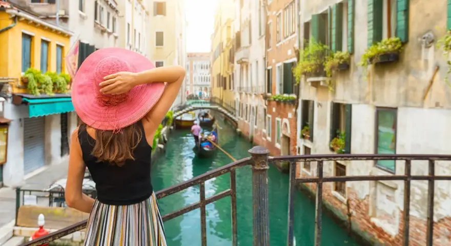 Una donna con cappello rosa ammira un canale a Venezia, un'esperienza indimenticabile di "Venezia in un giorno a piedi".