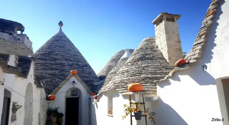 Trulli con zucche arancioni nel centro storico di Alberobello, sotto un cielo azzurro.