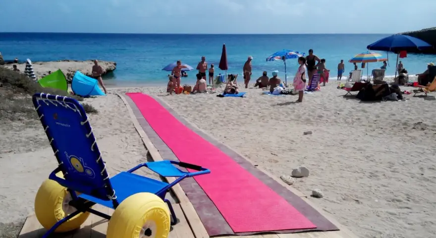 Una spiaggia attrezzata per gite per disabili, con una passerella rosa e una sedia a rotelle speciale per la sabbia.