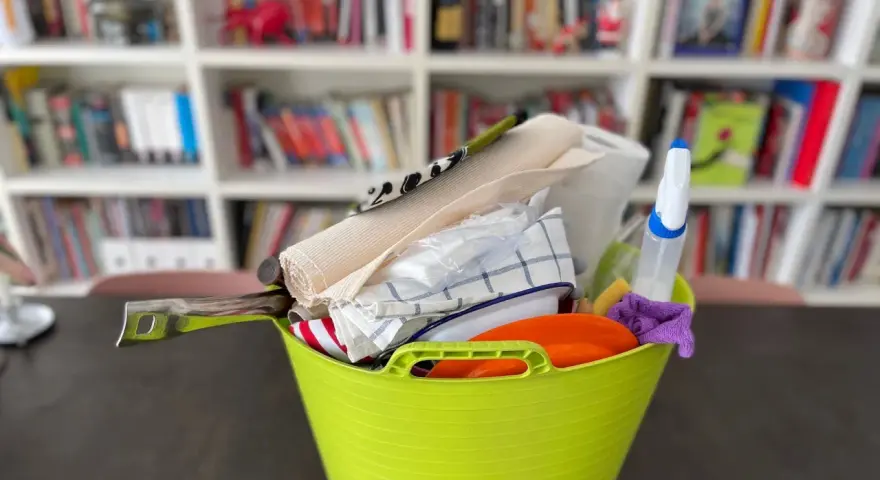 Secchio verde con accessori per la pulizia: rotolo di carta, panni, spruzzino, spugna. Ideale per sapere cosa portare in camper per un viaggio pulito.