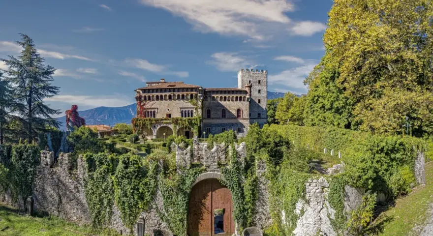 Villa d'Ayala, un castello incantevole con torri e giardini lussureggianti, immerso tra le montagne sotto un cielo azzurro.