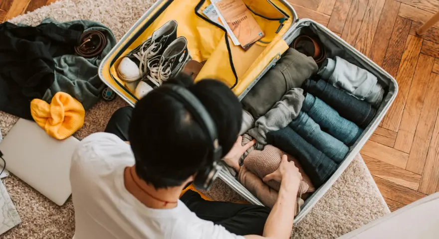 Preparazione per la gita: valigia aperta con vestiti piegati, scarpe, cintura, cappello giallo e laptop.