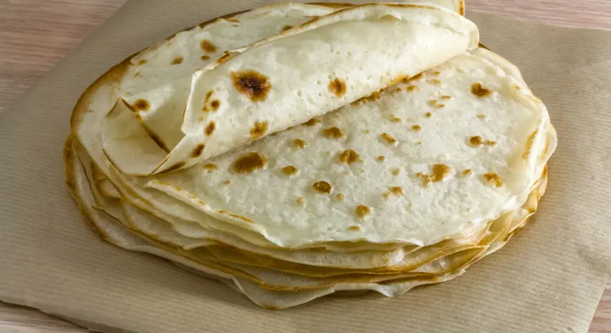 Impasto piadina appena cotto, impilato su carta da forno. Le sottili sfoglie dorate invitano a essere farcite.