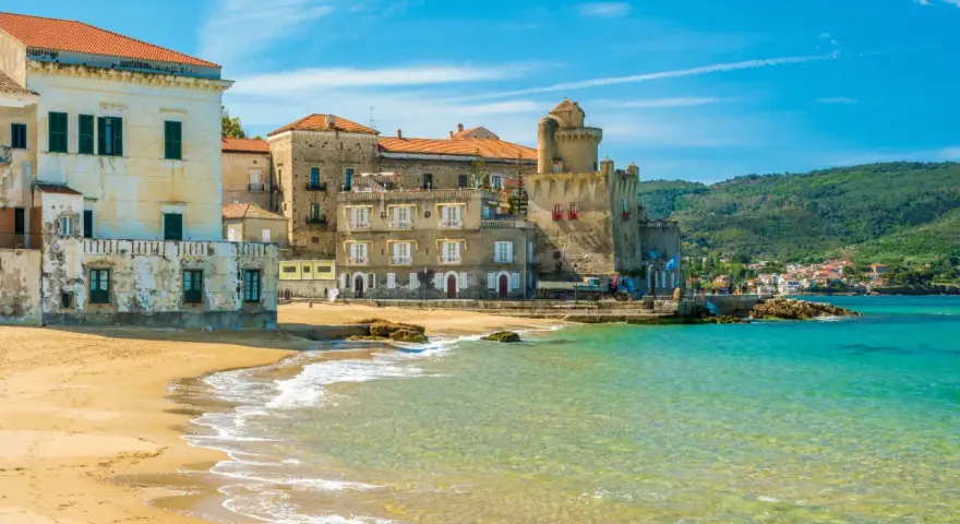 Spiaggia dorata e mare cristallino a Castellabate, con antichi palazzi e un castello che si affacciano sull'acqua. Un posto al mare da sogno.