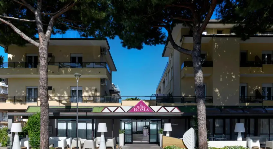 Hotel Roma Cesenatico, con pini marittimi e arredi esterni moderni, invita al relax.