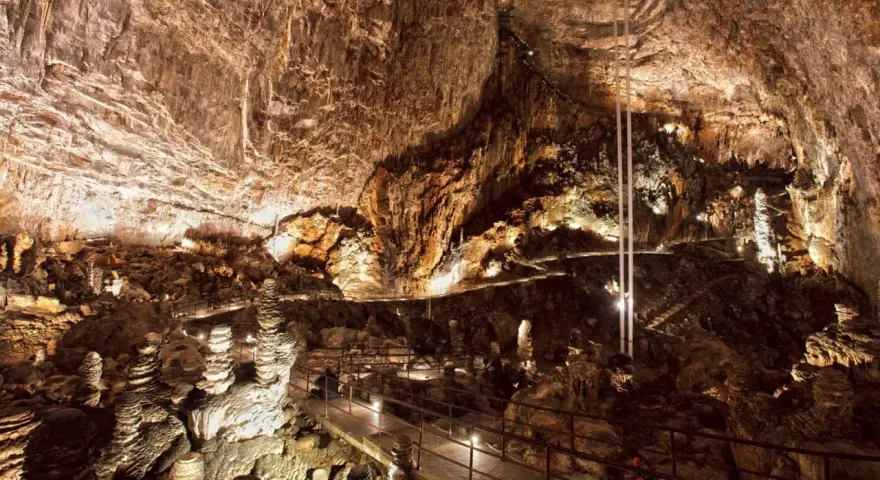 Sentiero illuminato tra stalattiti e stalagmiti in una delle magnifiche grotte in Italia. Un viaggio sotterraneo mozzafiato.