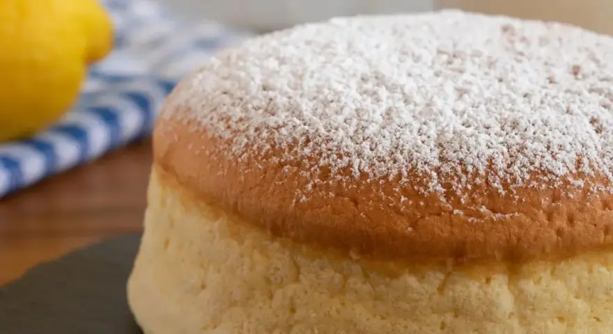 Torta al vento mantovana soffice e leggera, cosparsa di zucchero a velo. Accanto, un limone e un tovagliolo a righe blu.
