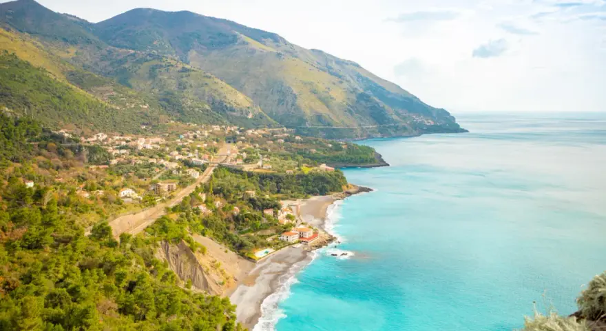 Panoramica di una costa montuosa con un villaggio affacciato sul mare turchese. Perfetto per itinerari Basilicata in macchina.