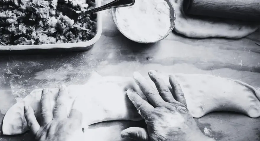 Mani esperte modellano la pasta per creare un'azdora romagnola, con ripieno e farina pronti.