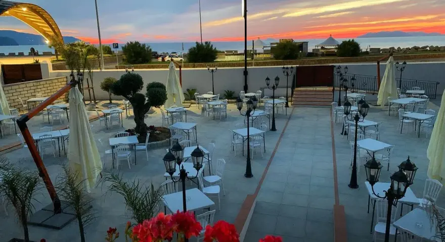 Terrazza di un ristorante al tramonto, con tavoli apparecchiati e fiori rossi. Un invito a scoprire il **vecchio palmento menu**.