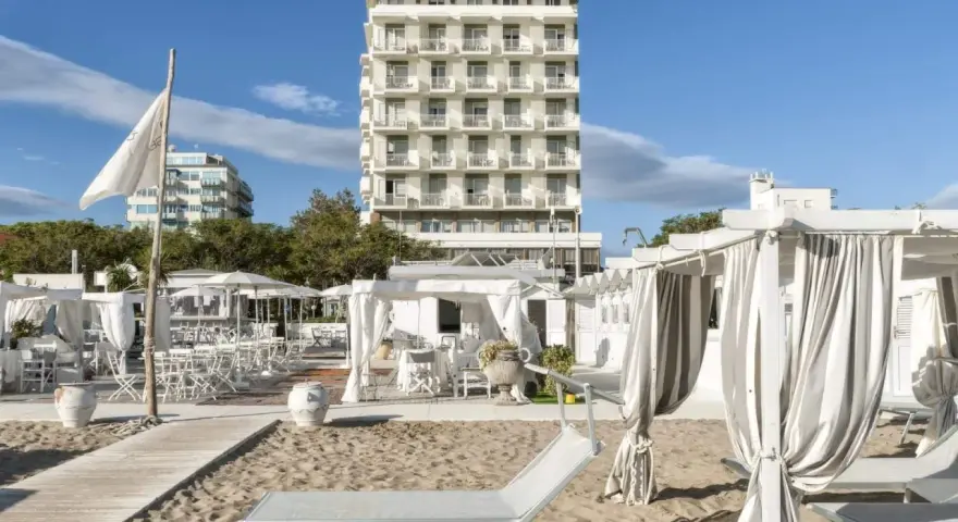 Spiaggia attrezzata con lettini e gazebo bianchi, sullo sfondo l'imponente hotel Abners.