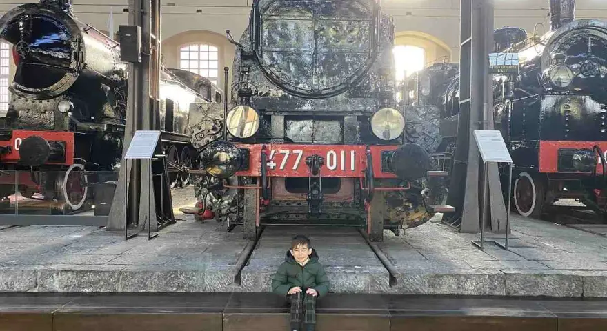 Bambino seduto davanti a un imponente treno storico al Museo di Pietrarsa, Napoli.