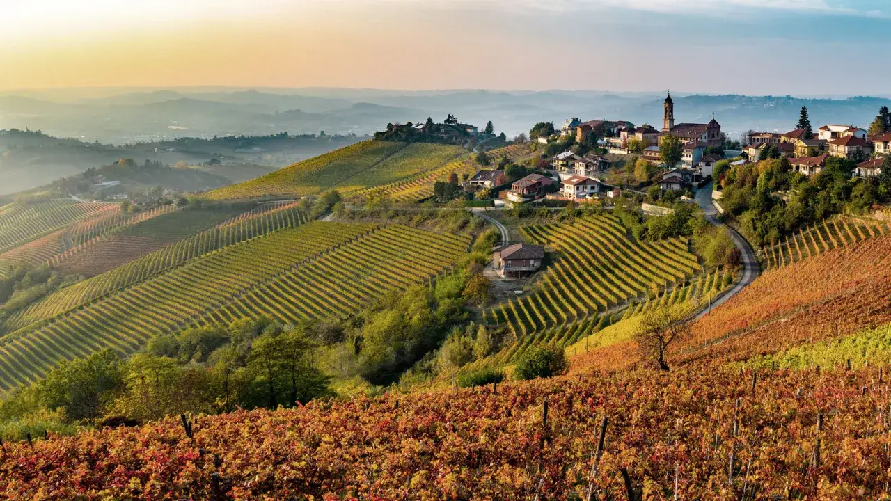 Dolci colline del Piemonte in autunno, con vigneti colorati e un borgo. Ideale per esplorare i percorsi enogastronomici Piemonte.