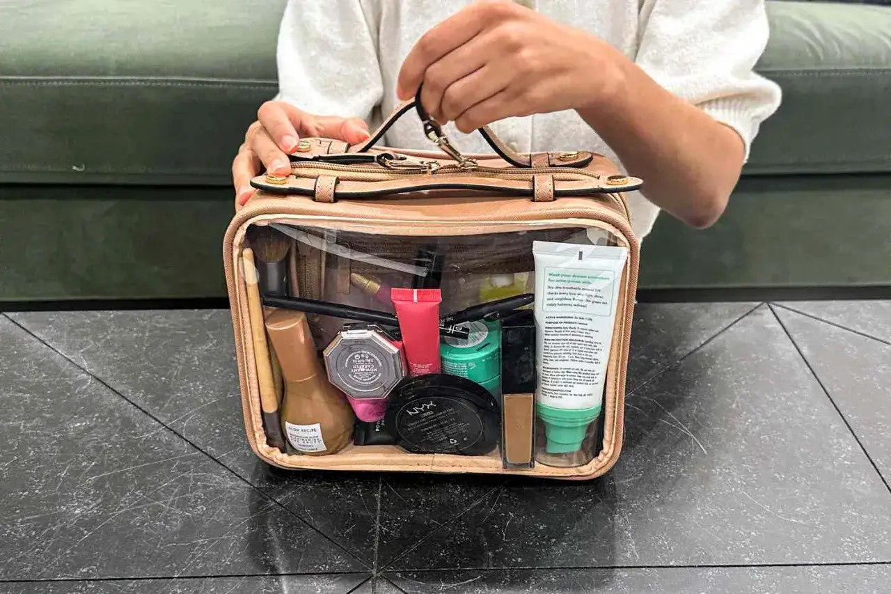 Un beauty case trasparente pieno di trucchi: fondotinta, cipria, rossetti, pennelli. Ideale per sapere cosa mettere nel beauty case per ogni occasione.