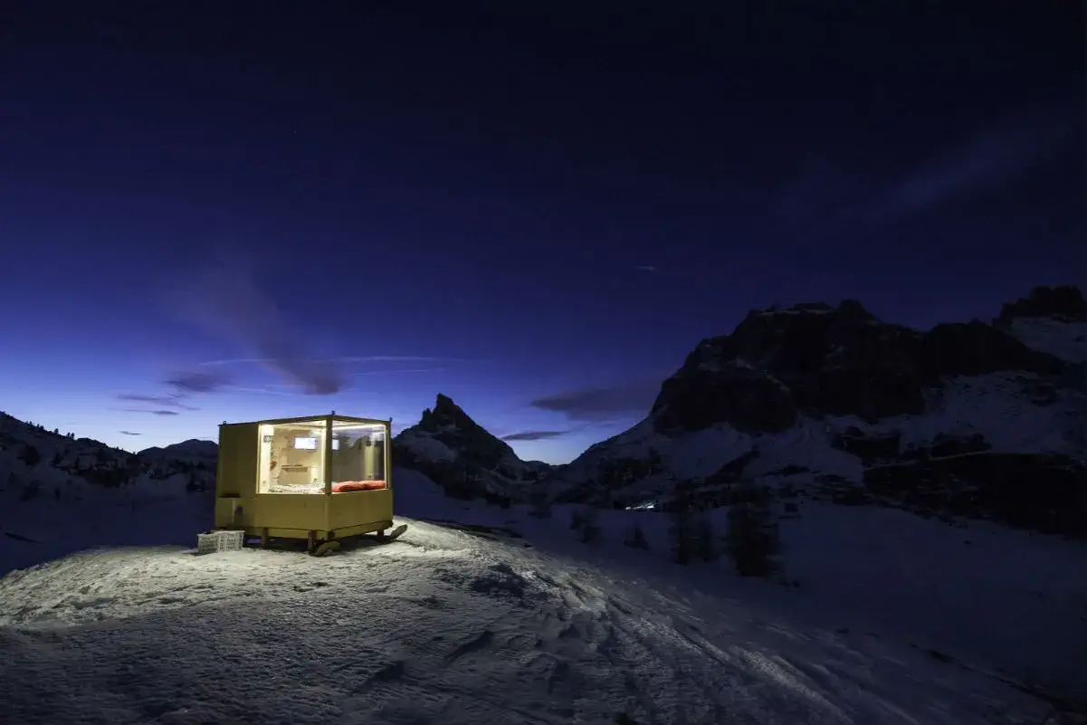 Un rifugio moderno per dormire in un igloo in Italia, illuminato nella notte alpina, con montagne innevate sullo sfondo.
