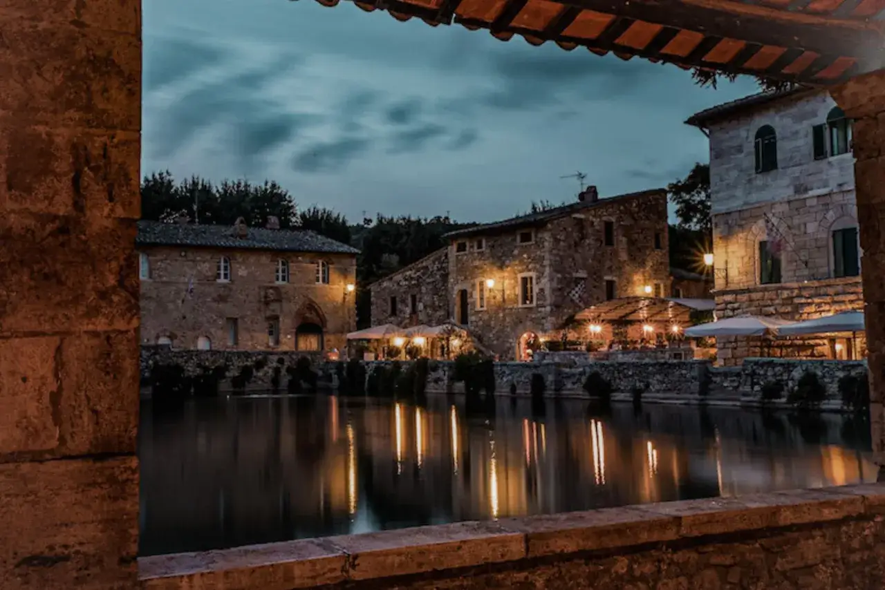 Un suggestivo weekend nel centro Italia: antichi borghi in pietra illuminati da luci calde si specchiano in un laghetto tranquillo.