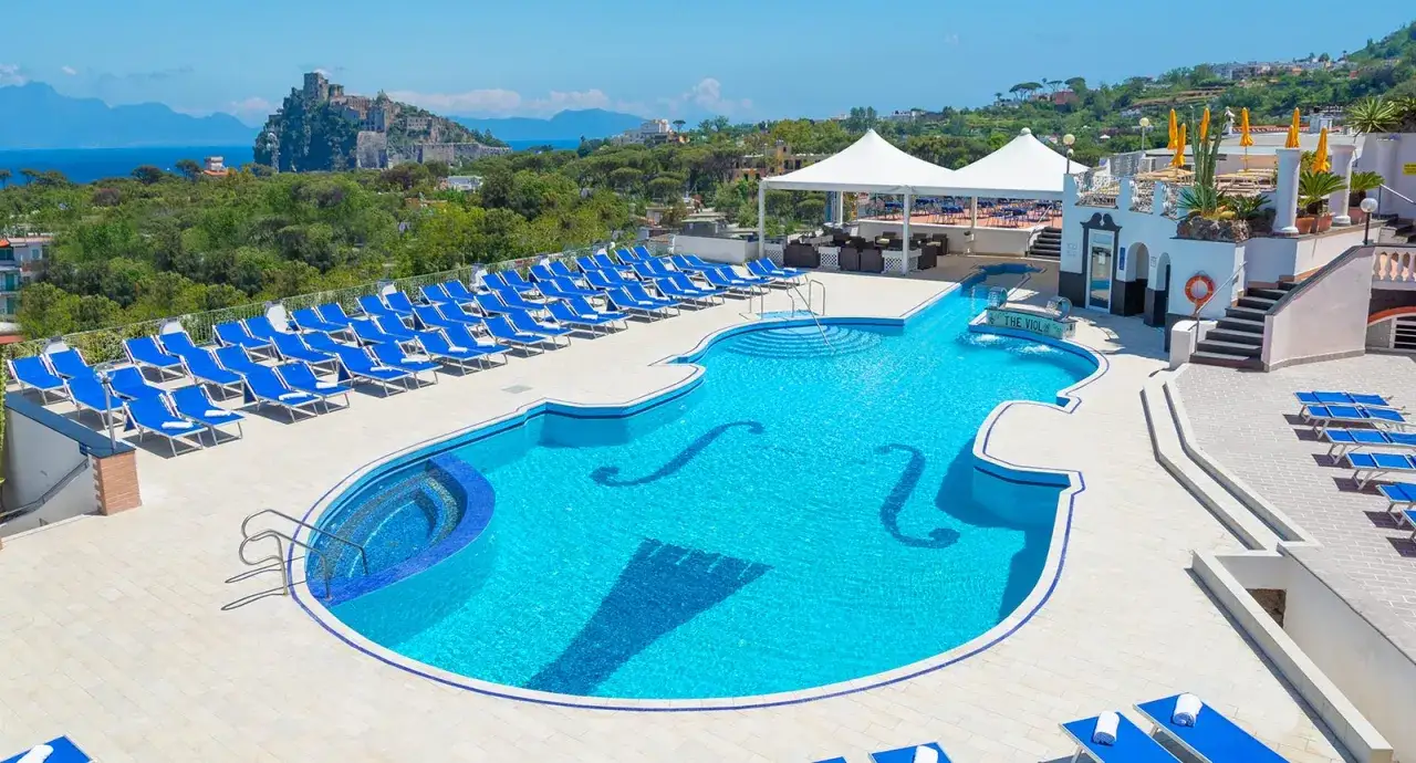Piscina a forma di violino con lettini blu e vista sul castello, presso l'hotel terme tramonto d'oro Ischia.
