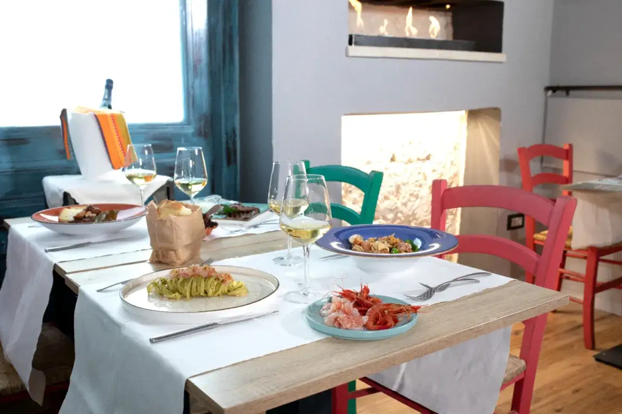 Tavola apparecchiata con piatti di pasta, gamberi e vino alla trattoria Angiolino Lecce.