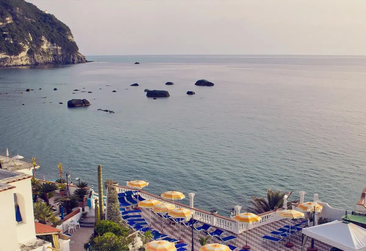Vista mare dal hotel tramonto Ischia: lettini, ombrelloni e scogli in un'atmosfera serena.