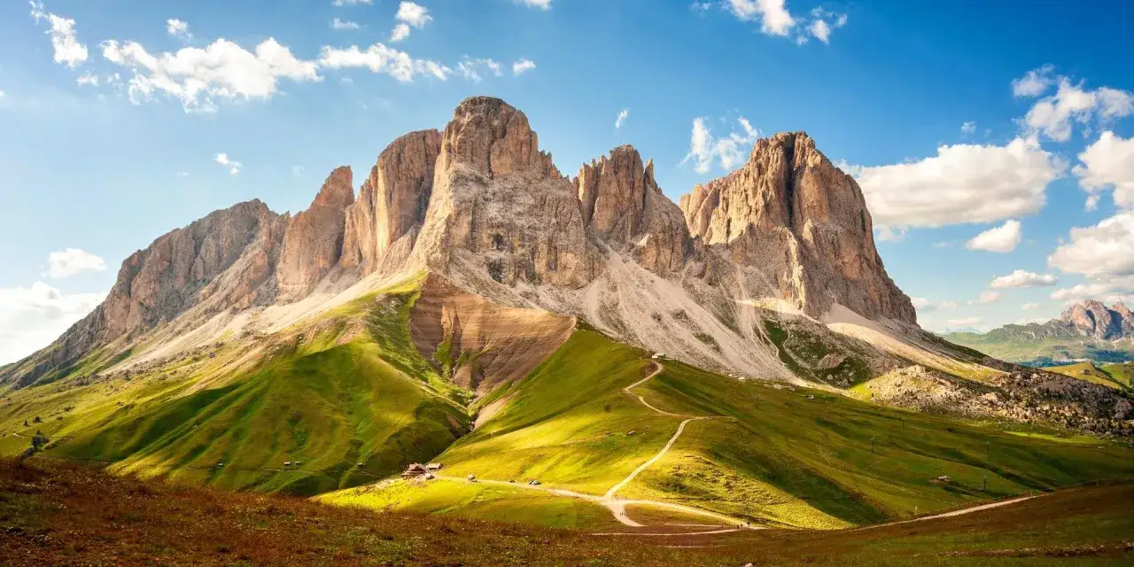 Sentiero panoramico tra verdi colline e imponenti vette rocciose, ideale per scoprire cosa fare a Canazei.