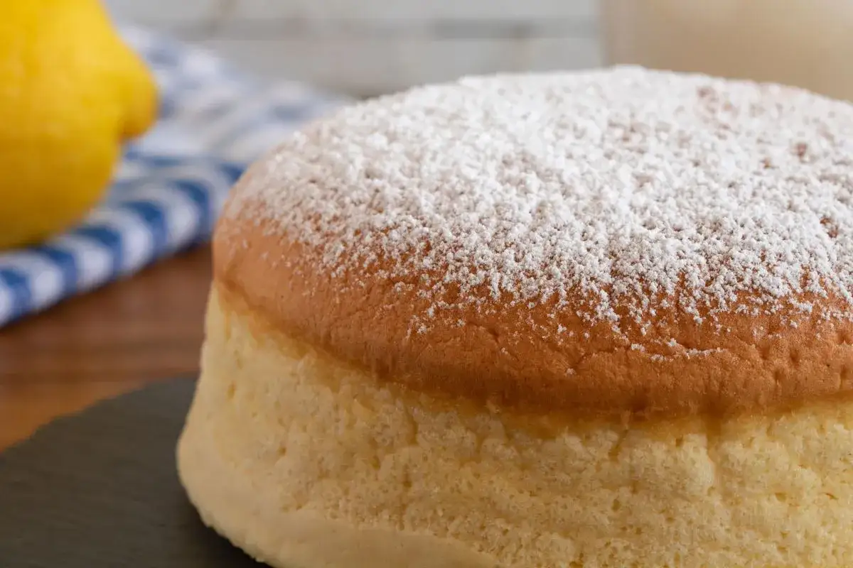 Una soffice torta al vento mantovana, cosparsa di zucchero a velo, con limoni sullo sfondo.