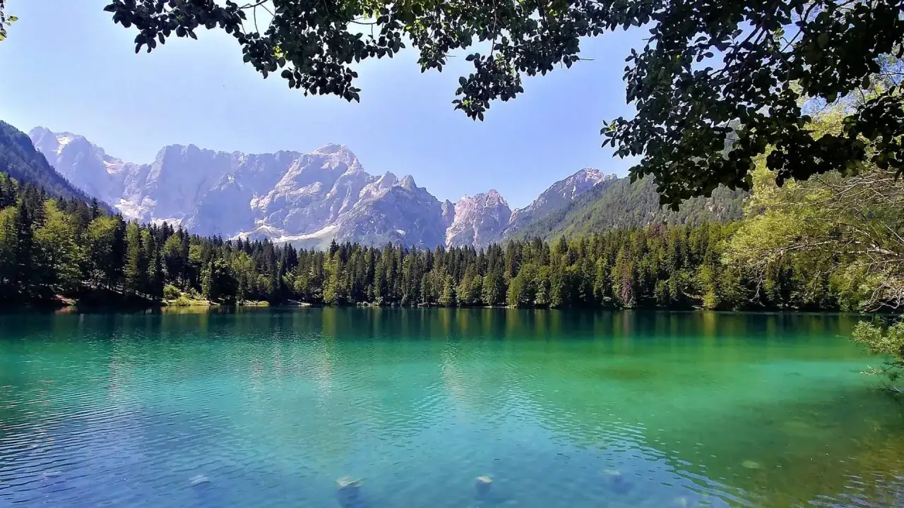 Lago di Fusine, uno dei posti da vedere a Tarvisio, con montagne maestose e foresta rigogliosa che si specchiano nelle acque cristalline.