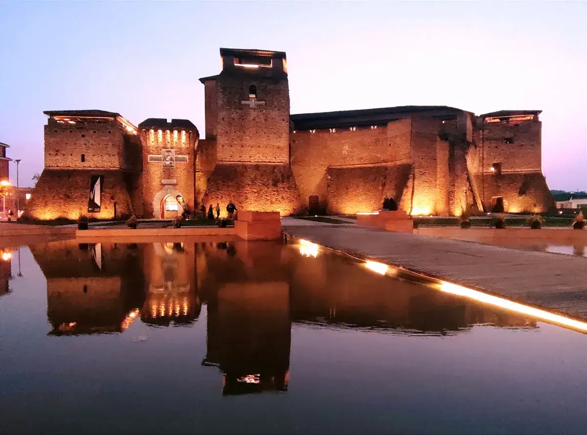 Castello illuminato di notte, riflesso sull'acqua. Un luogo magico che evoca il Fellini Museum.