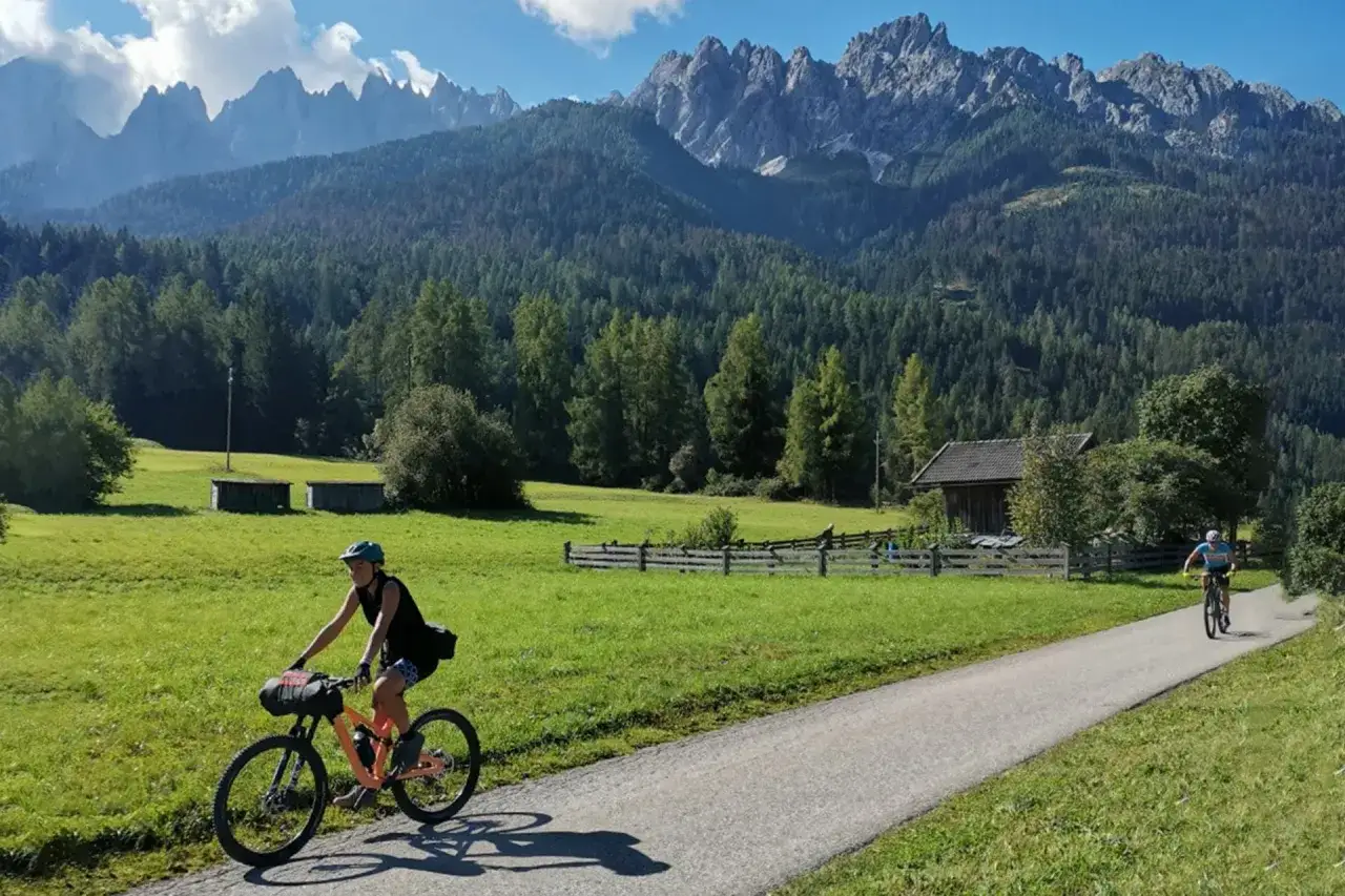 Ciclisti su una ciclabile panoramica, con montagne imponenti sullo sfondo. Un'avventura lungo la ciclabile San Candido Lienz km.