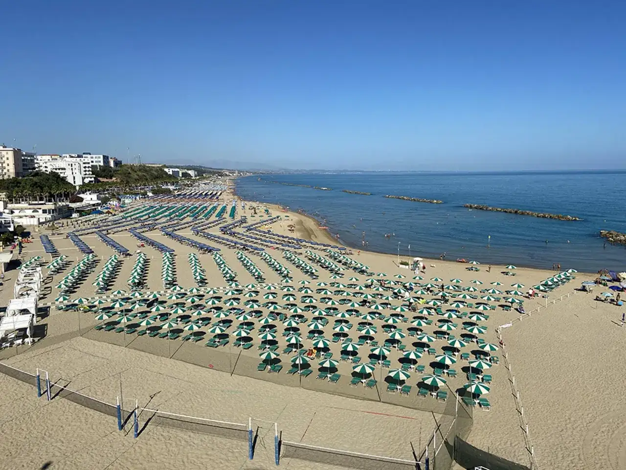 Ampia spiaggia attrezzata con file di ombrelloni verdi e bianchi, perfetta per scoprire cosa vedere vicino a Termoli. Mare azzurro e cielo sereno.