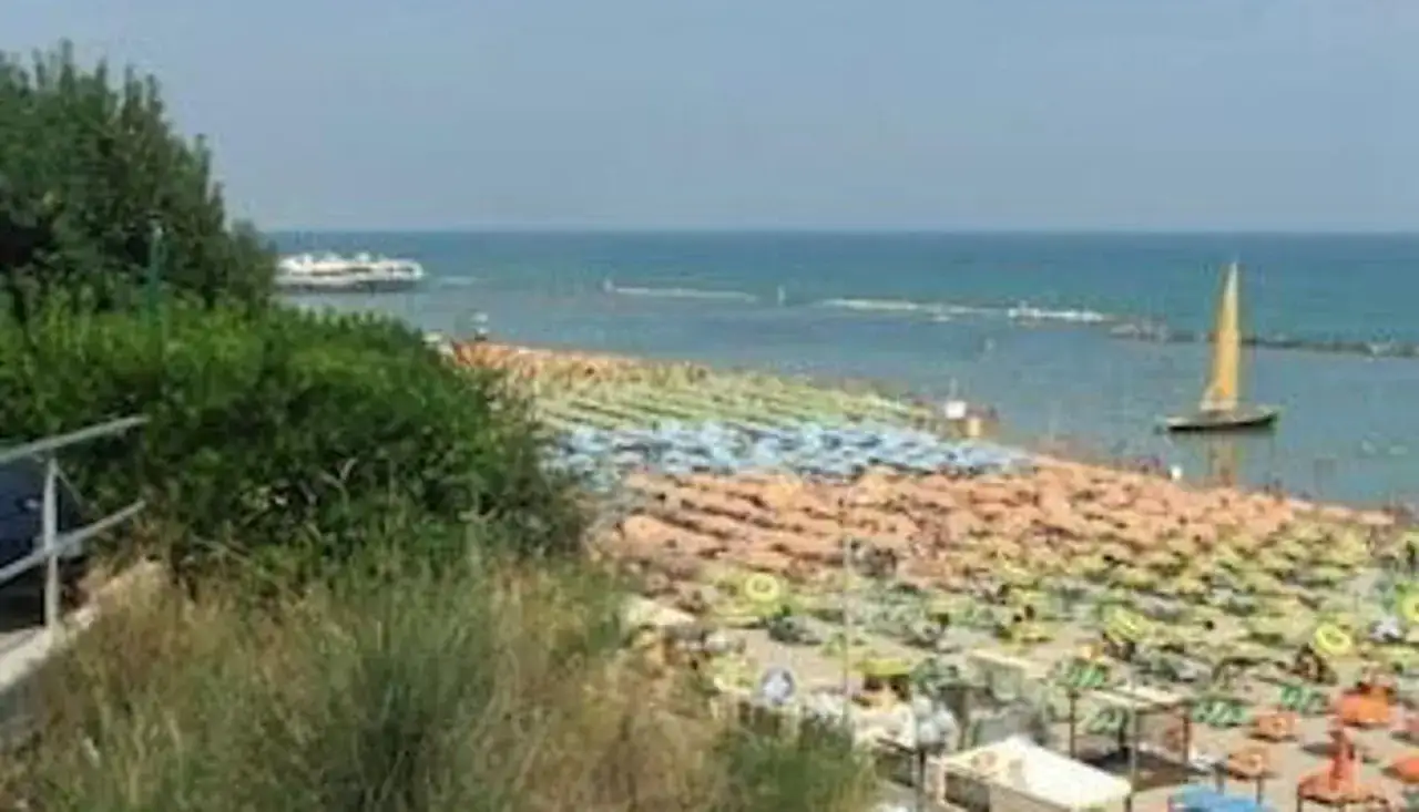 Spiaggia affollata con ombrelloni colorati e un veliero al largo, vista panoramica dal hotel Plaza Gabicce Mare.