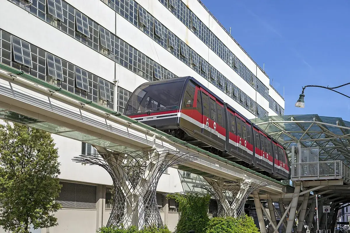 Un treno rosso e nero sfreccia su un binario sopraelevato, con un edificio moderno sullo sfondo. Un viaggio da tronchetto a piazza San Marco.