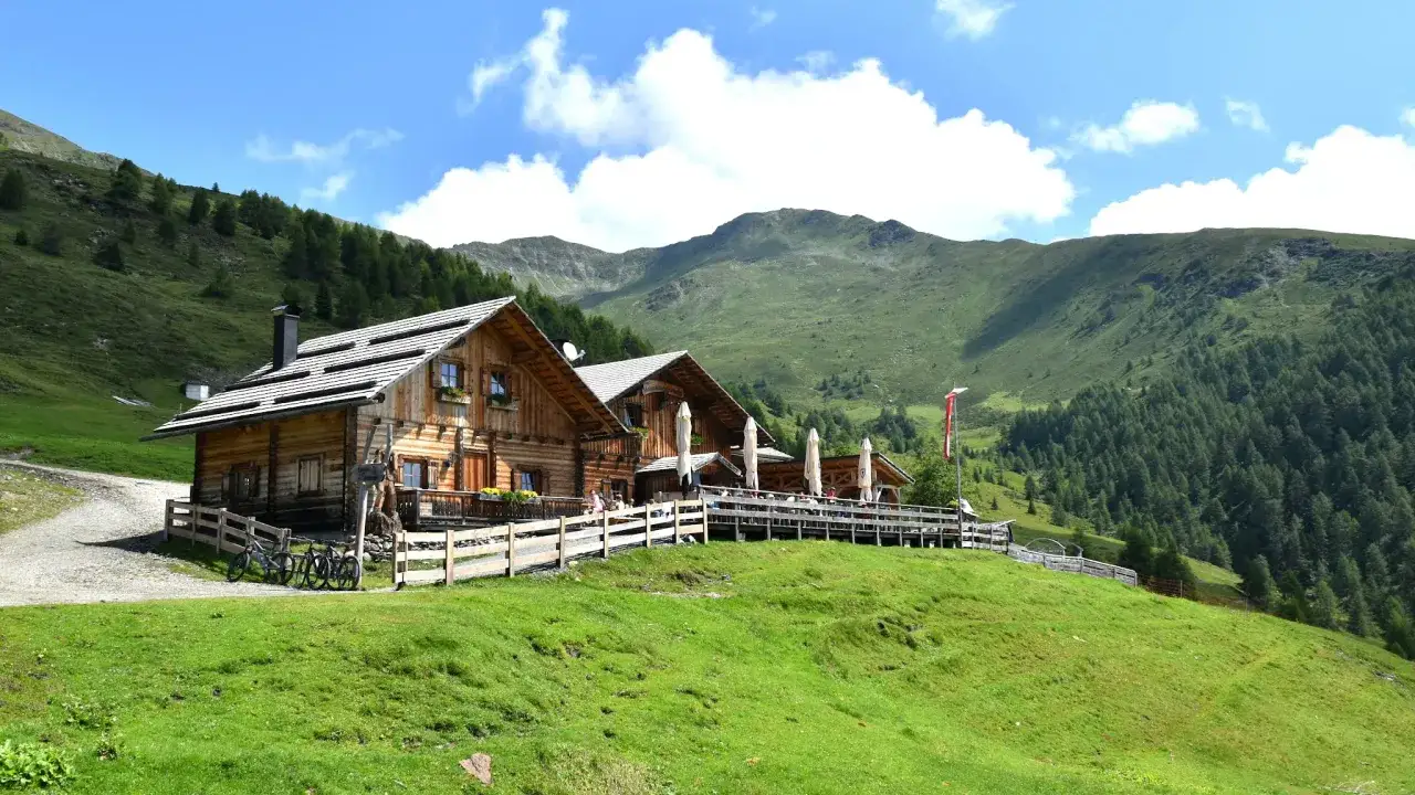 Rifugio in legno in Friuli, montagna in estate, con ciclisti che riposano e un panorama mozzafiato.