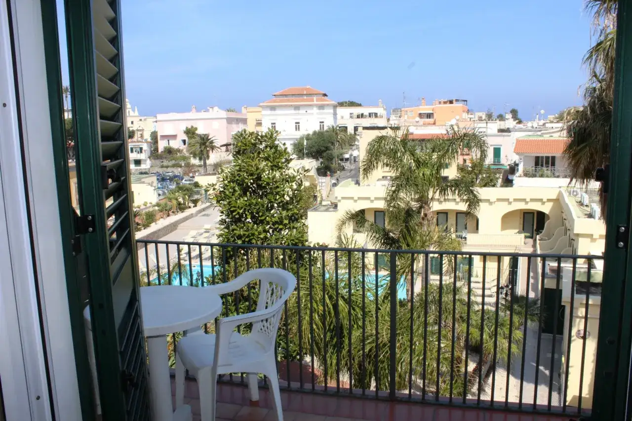 Vista dal balcone dell'hotel Punta del Sole a Ischia: piscina, palme e tetti colorati.
