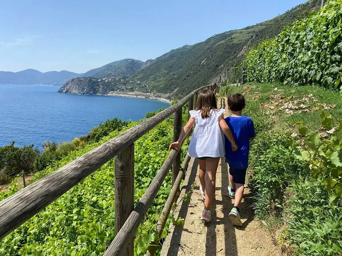 Bambini esplorano i sentieri panoramici delle Cinque Terre, con il mare blu e la vegetazione rigogliosa.