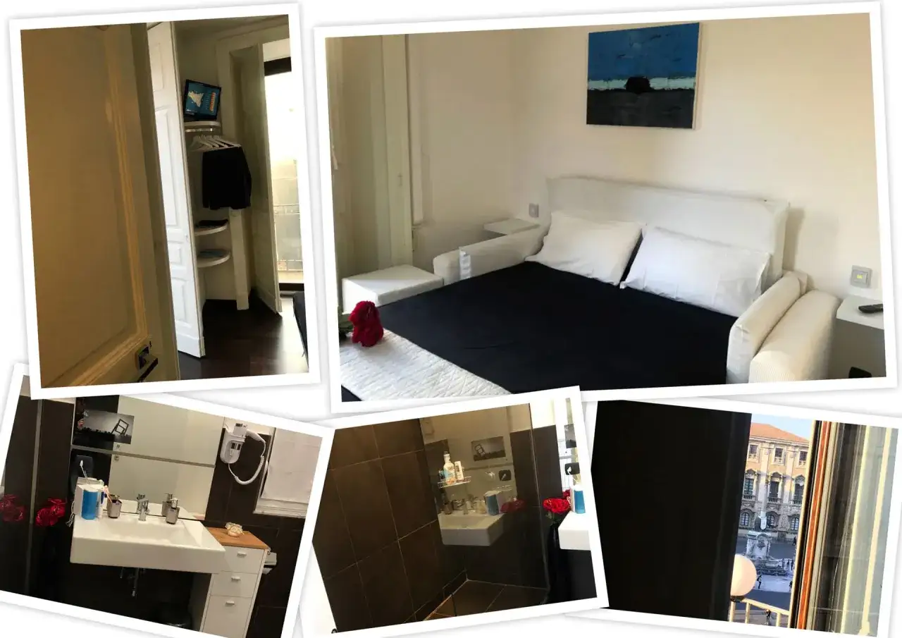 Interno di un albergo una stella: letto matrimoniale con lenzuola nere, bagno con lavandino e specchio, armadio a muro e vista su un palazzo storico.