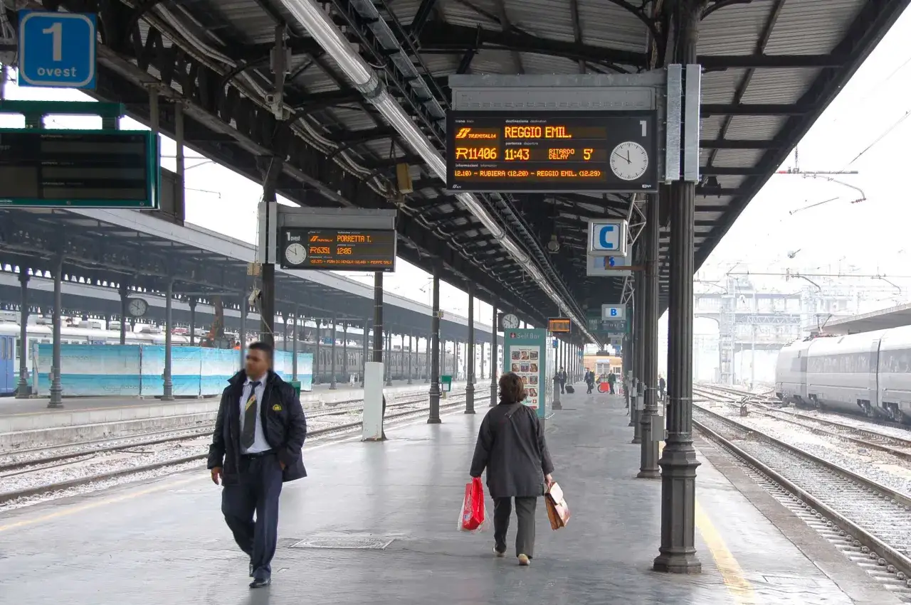 In stazione, controlla i tabelloni per capire come si prende un treno. Le indicazioni mostrano destinazione, orario e binario.