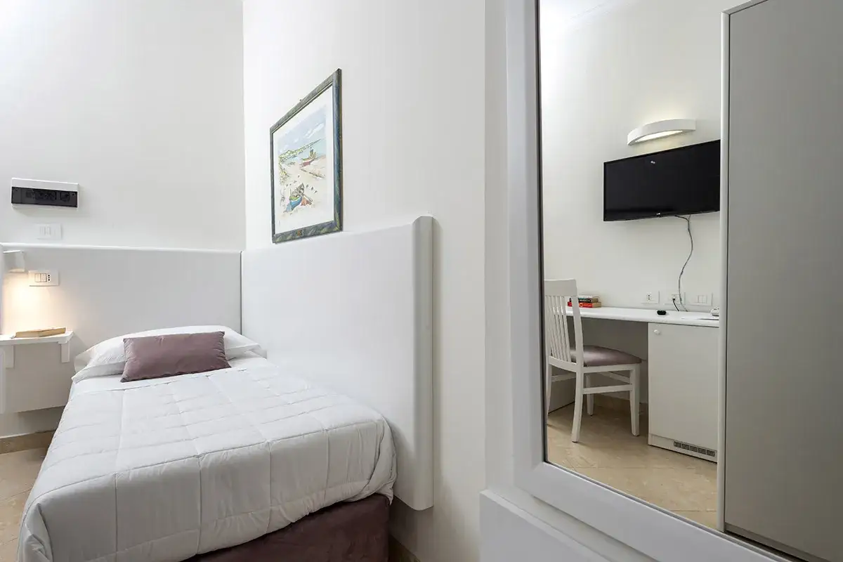 Accogliente camera singola hotel con letto, scrivania e TV visibile nello specchio.