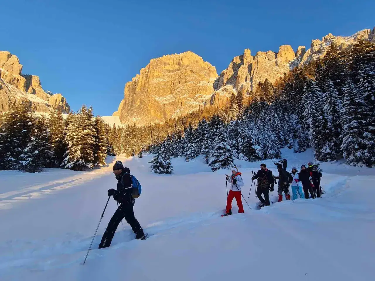 Gruppo di escursionisti con racchette da neve in un paesaggio innevato, con montagne illuminate dal sole. Un'ottima idea per cosa fare a Canazei in inverno.