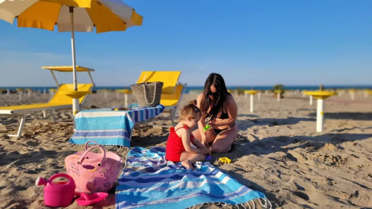 Mamma e bimba giocano sulla sabbia, con asciugamano 