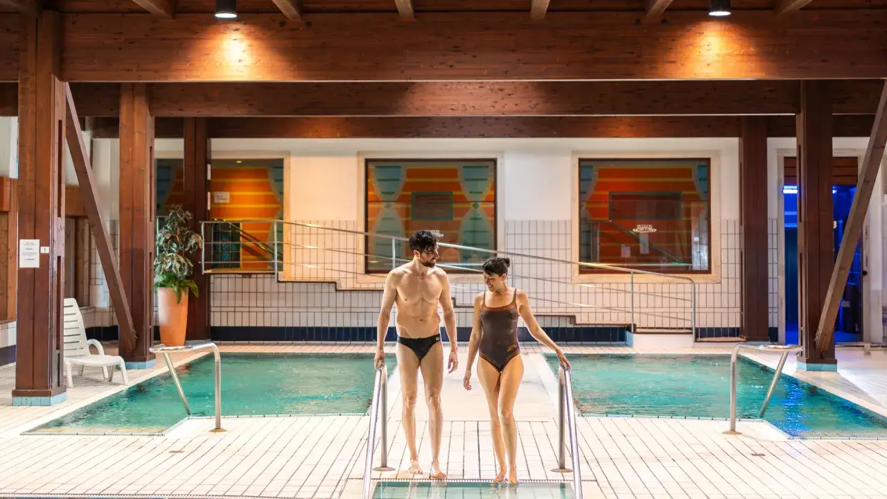 Coppia felice scende le scale di una piscina interna, godendosi un momento di relax alla fonte Riccione.