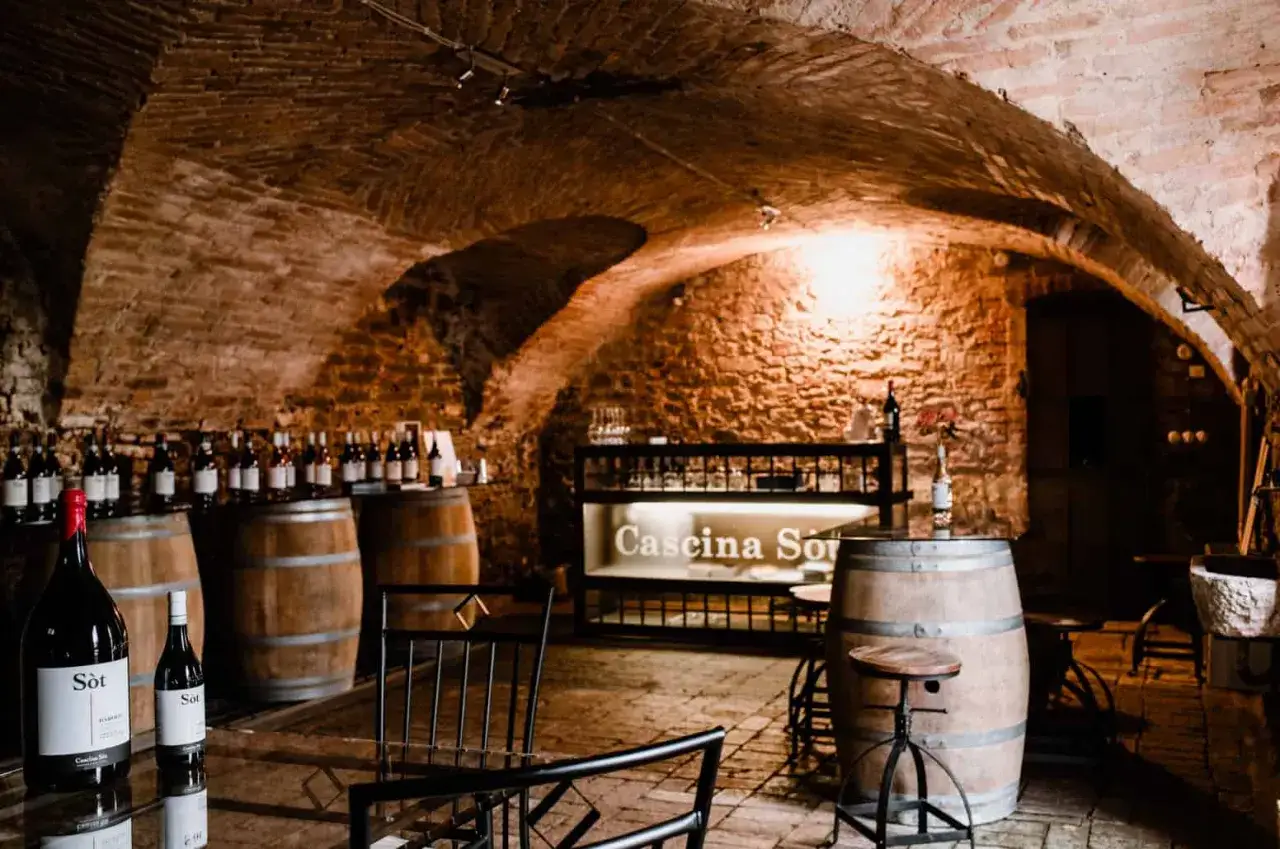 Cantina piemontese con botti di legno, bottiglie di vino e un'insegna luminosa