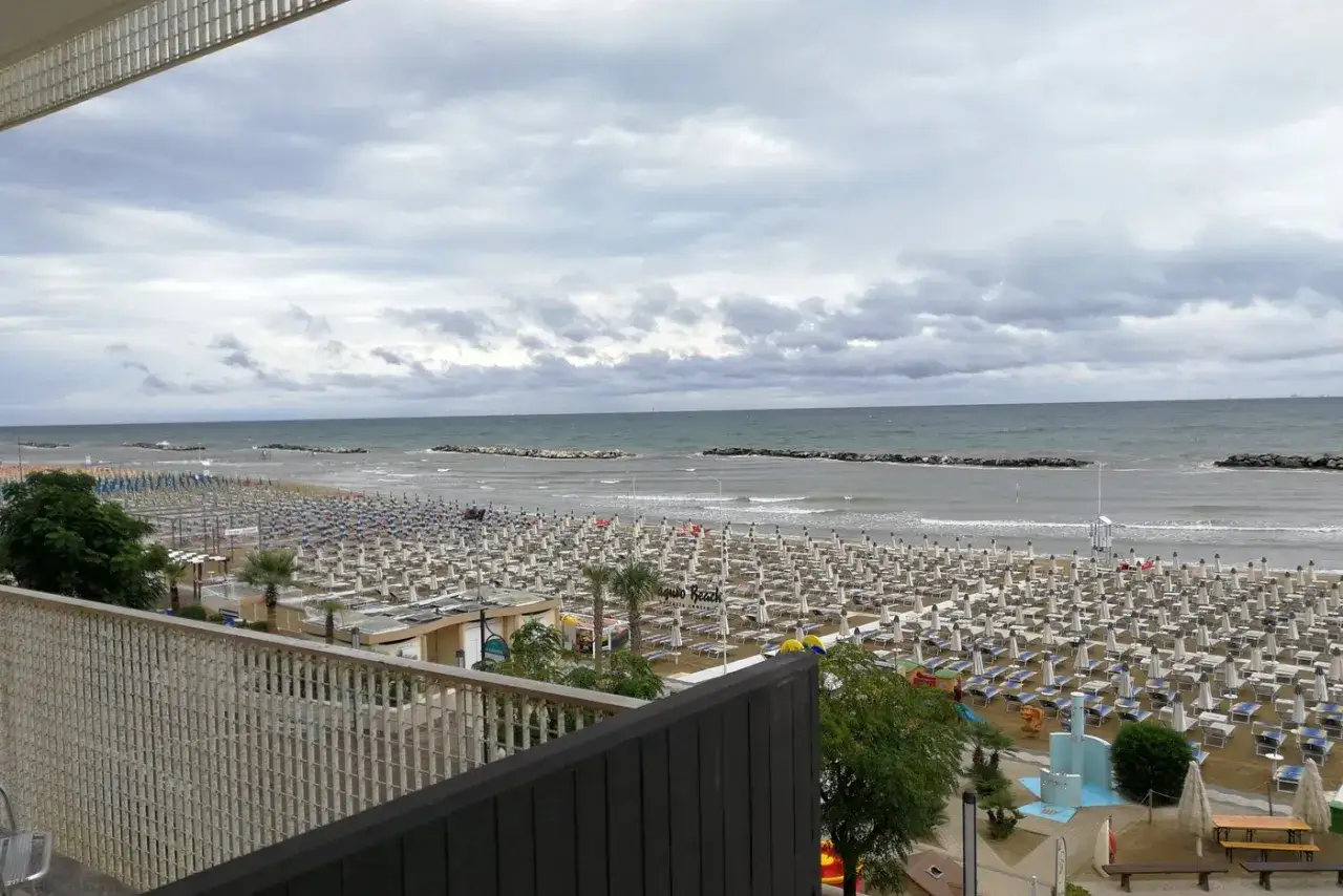 Spiaggia affollata di lettini e ombrelloni, con il mare calmo e il cielo nuvoloso. Vista dal piccadilly hotel bellaria.