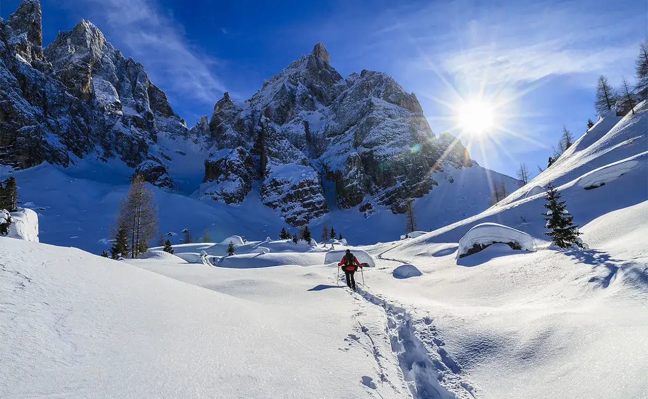Passeggiata invernale tra le montagne innevate, un'idea su cosa fare a Canazei. Sole splendente e sentiero battuto.