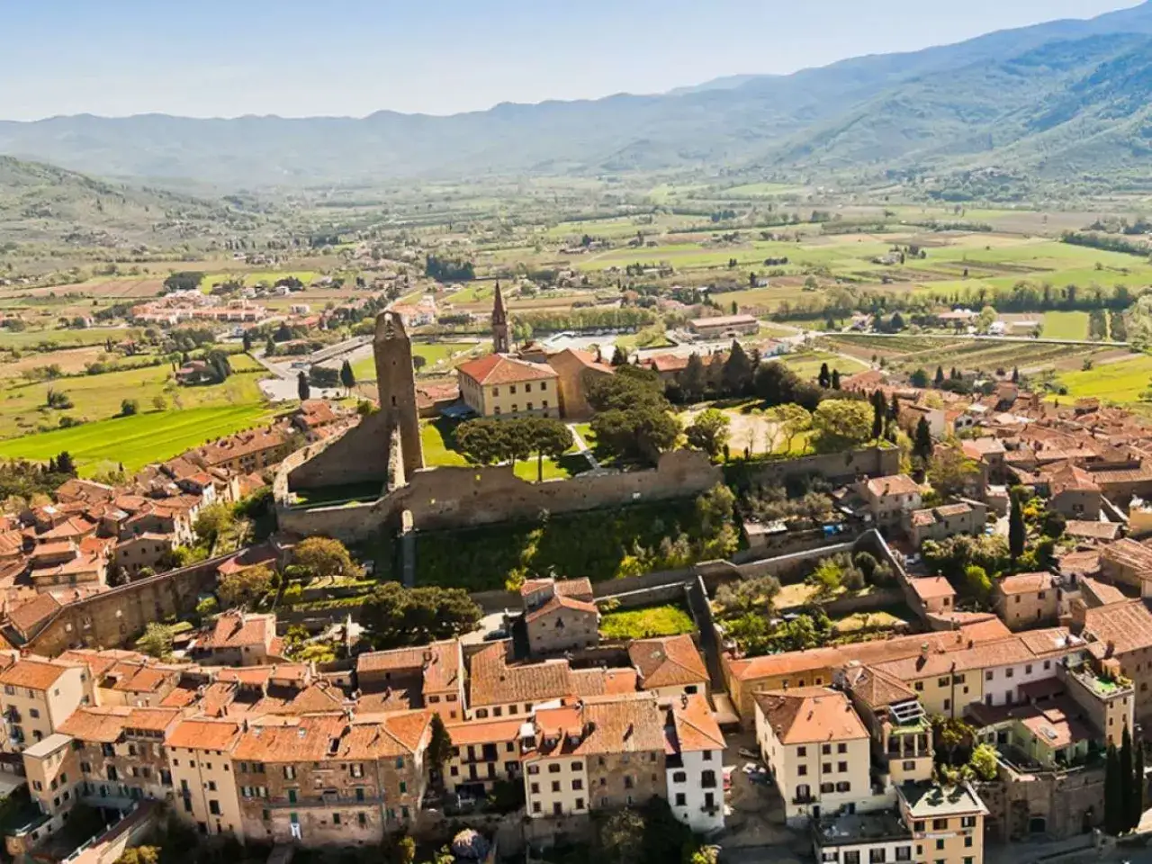 Un borgo medievale in collina, ideale per un tour Toscana 4 giorni. Case con tetti rossi e una torre imponente dominano il paesaggio verdeggiante.