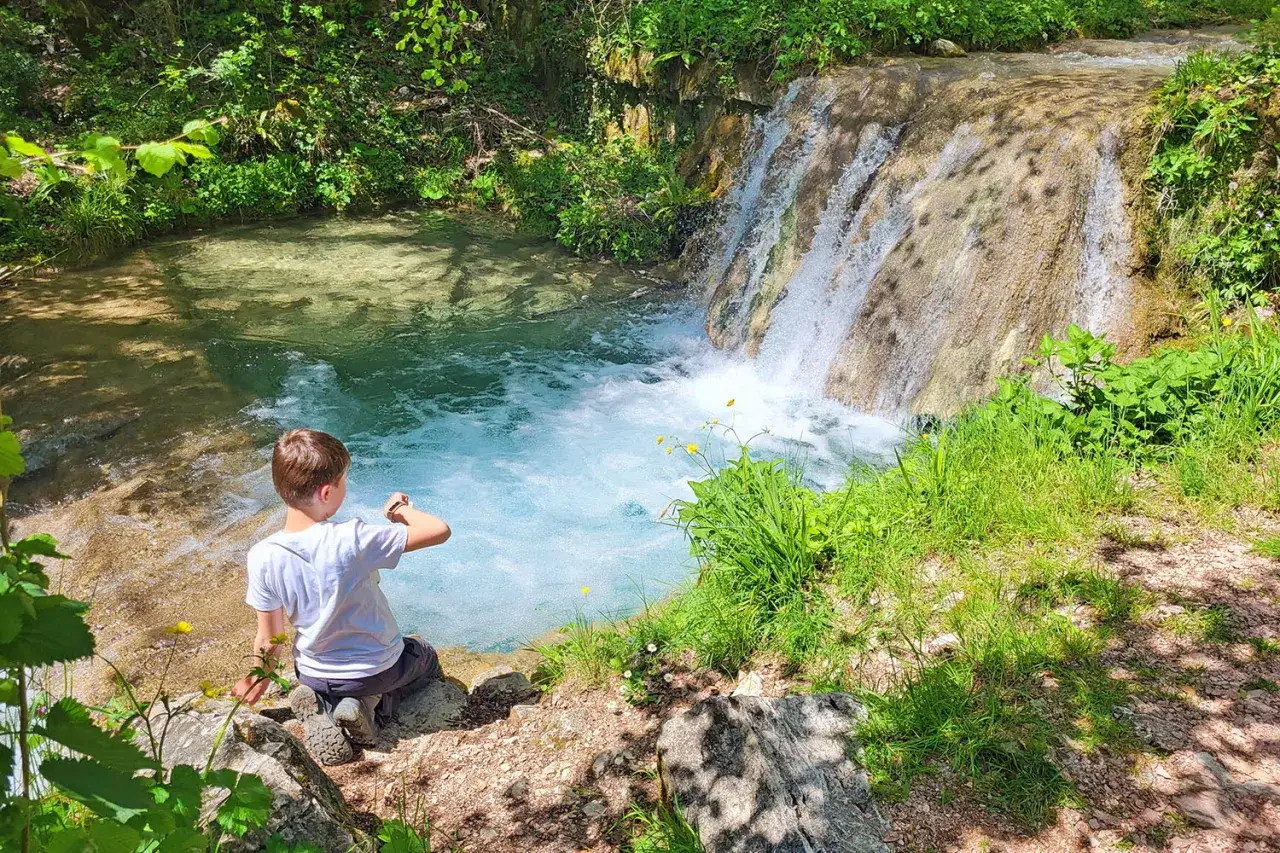 Bambino ammira una cascata durante una gita domenicale con bambini nel Lazio. L'acqua cristallina invita a un tuffo rinfrescante.