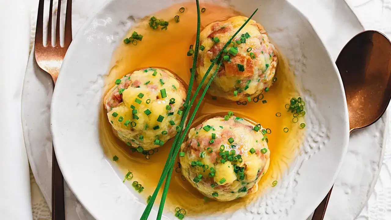 Tre canederli piatti tipici del Trentino Alto Adige, ricchi di speck e formaggio, serviti in un brodo dorato e guarniti con erba cipollina.