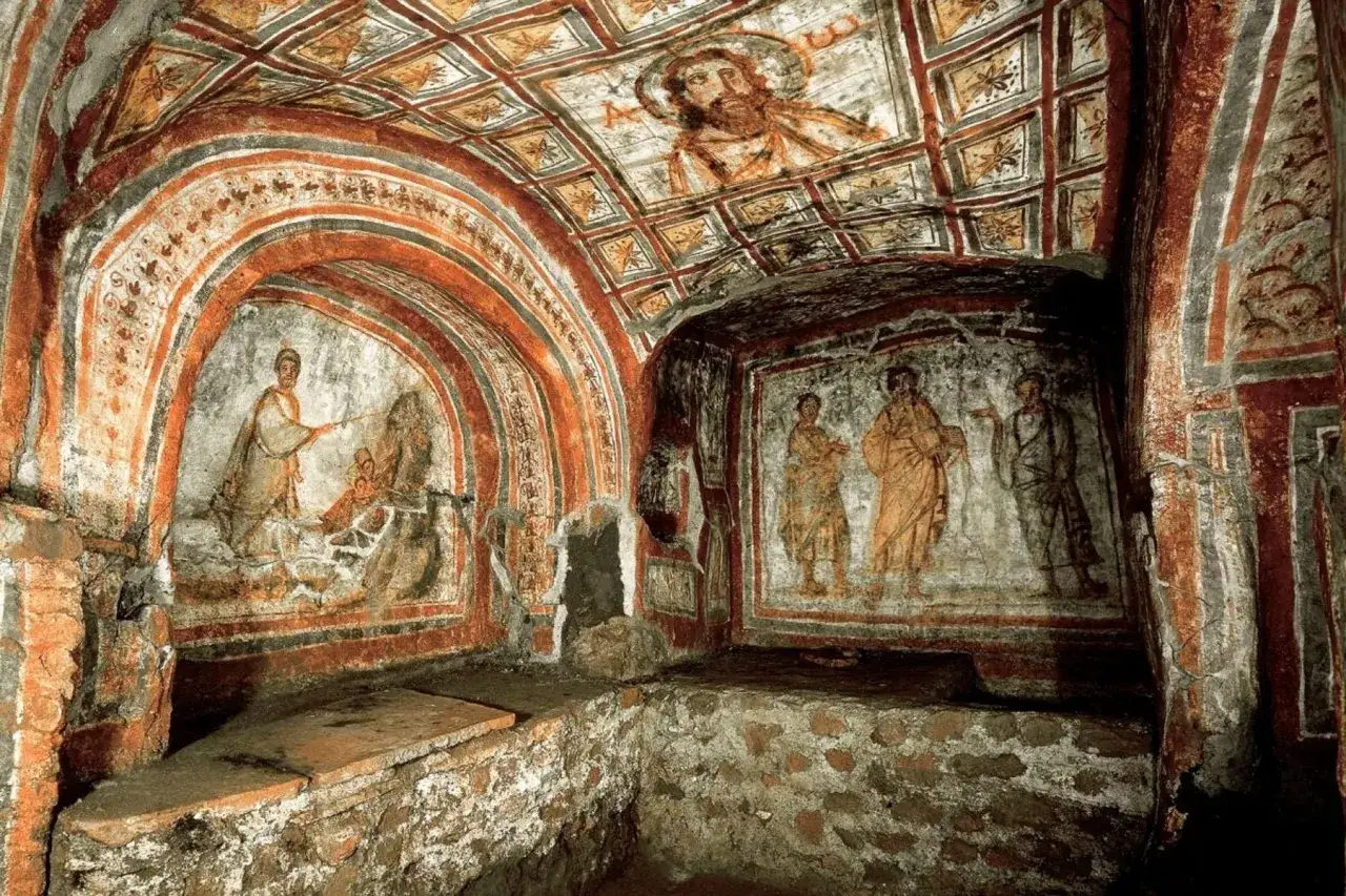 Affreschi antichi nelle catacombe di Roma più belle: un volto barbuto sul soffitto, scene bibliche e figure in toga.