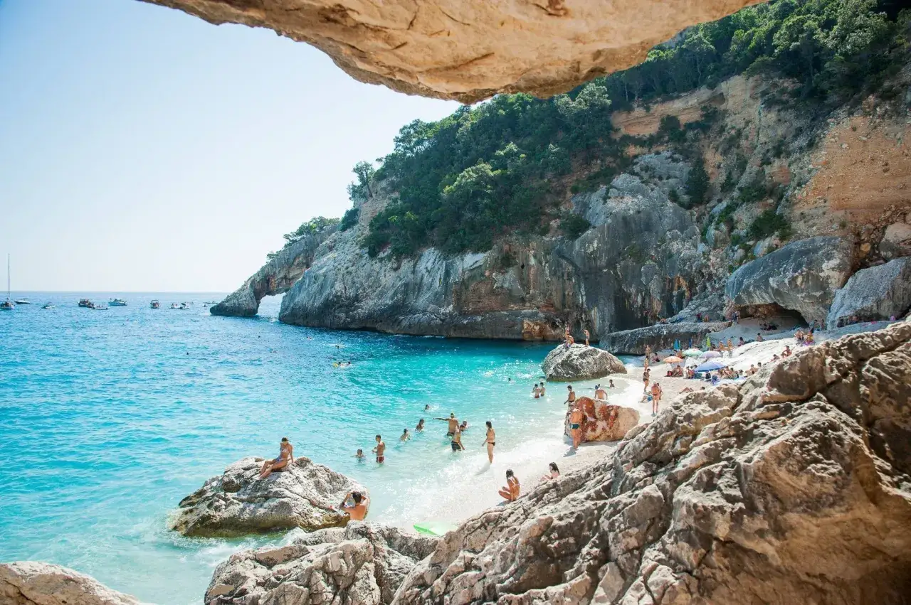 Spiaggia incantevole con acque turchesi, scogliere imponenti e gente che si gode il sole. Perfetta per le gite in Sardegna.