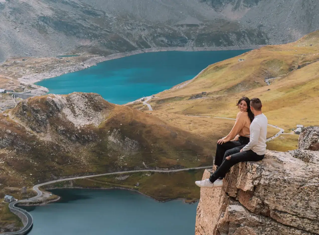 Coppia seduta su una roccia con vista su un lago alpino turchese. Un'idea perfetta per le gite in Piemonte.