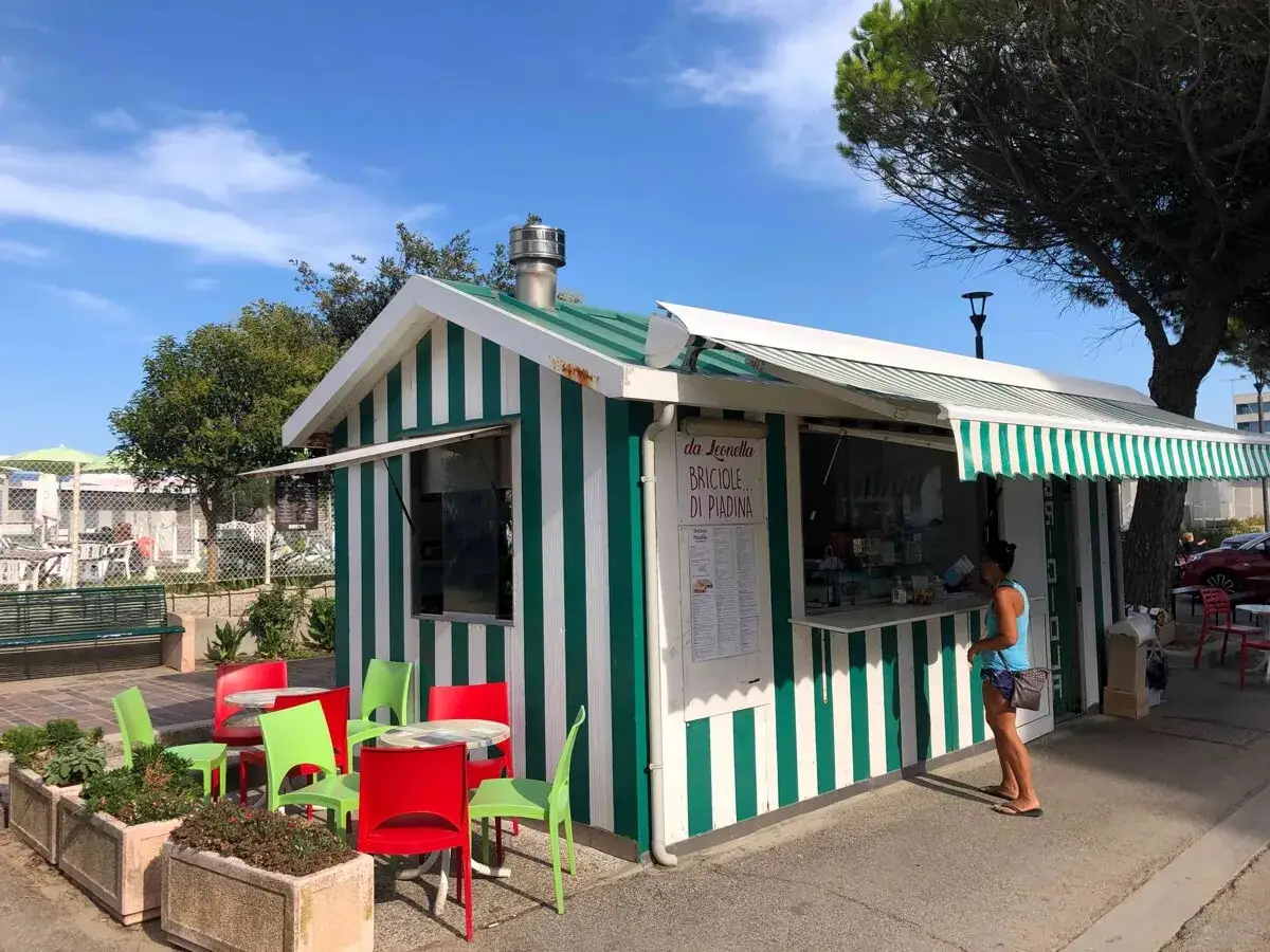 Chiosco a righe verdi e bianche, con tavolini e sedie colorate, dove si serve la piadina romagnola.